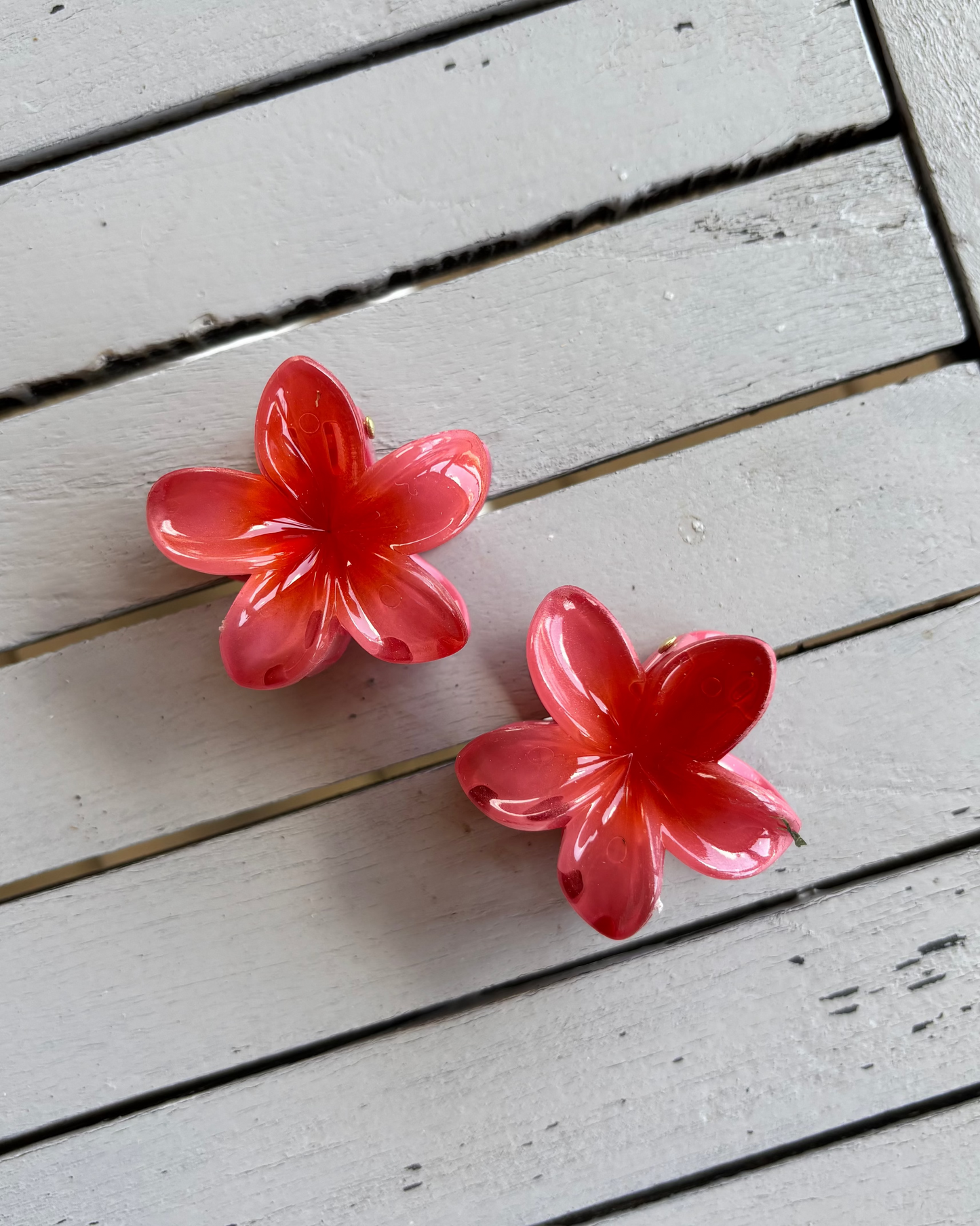 Two red flower-shaped hair clips on a wooden surface
