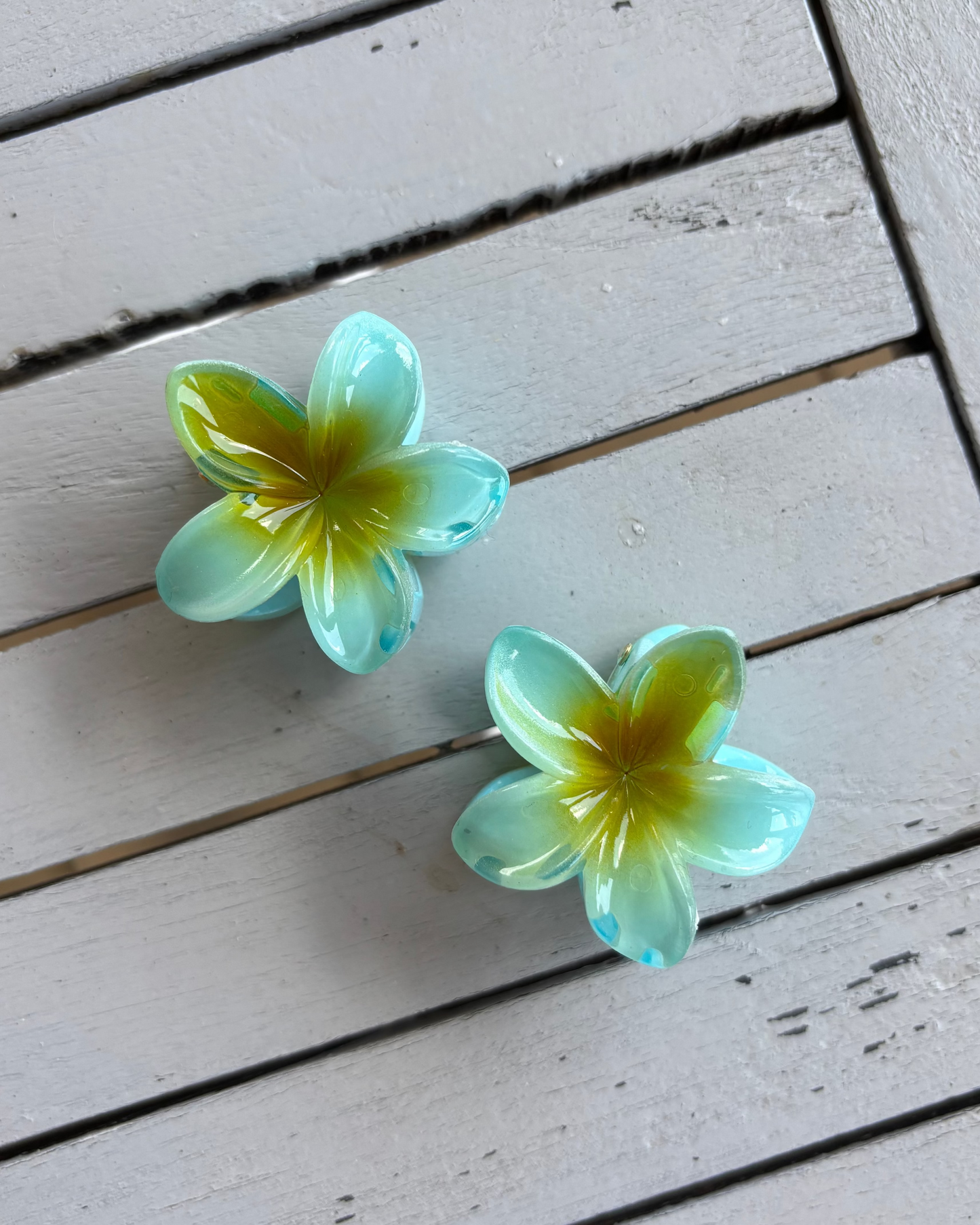 Two green and yellow flower-shaped hair clips on a wooden surface