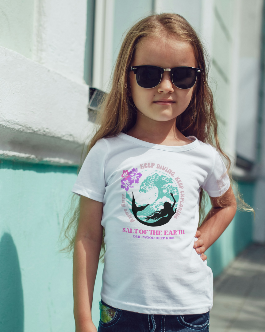 Young girl wearing a white t-shirt with a graphic design, standing against a light blue wall.