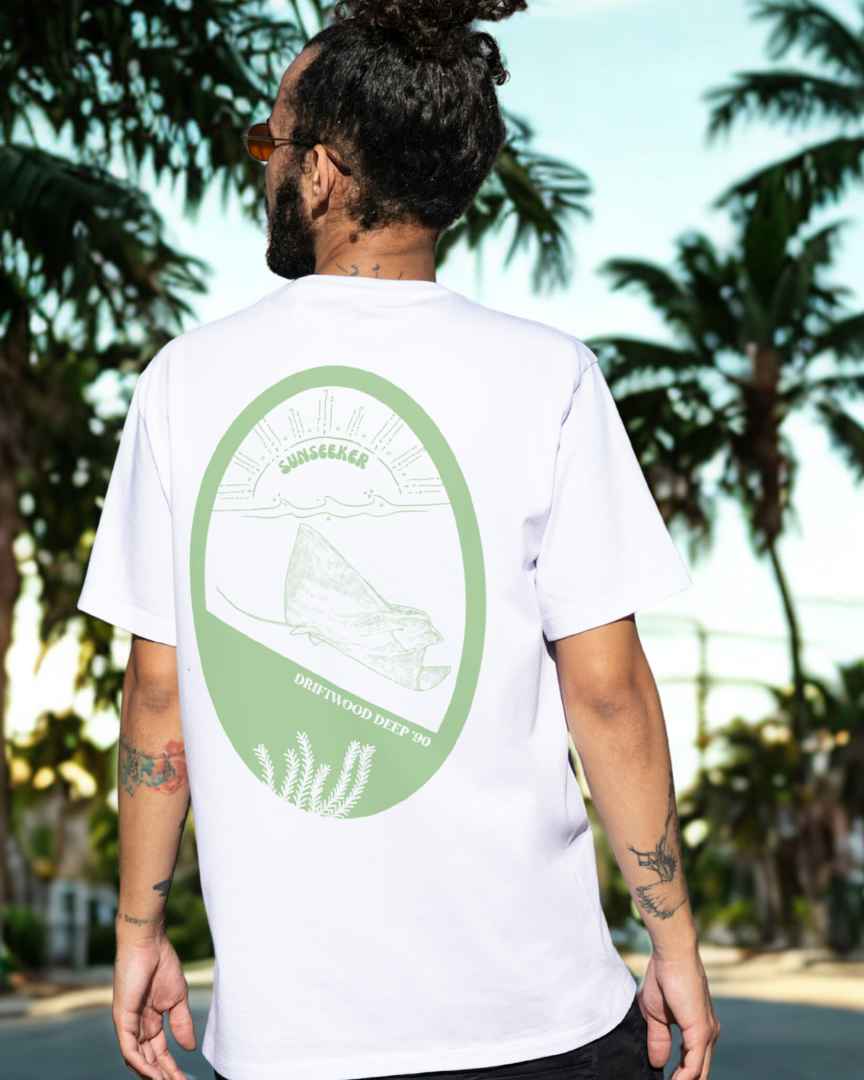 Person wearing a white t-shirt with a green logo in a tropical setting