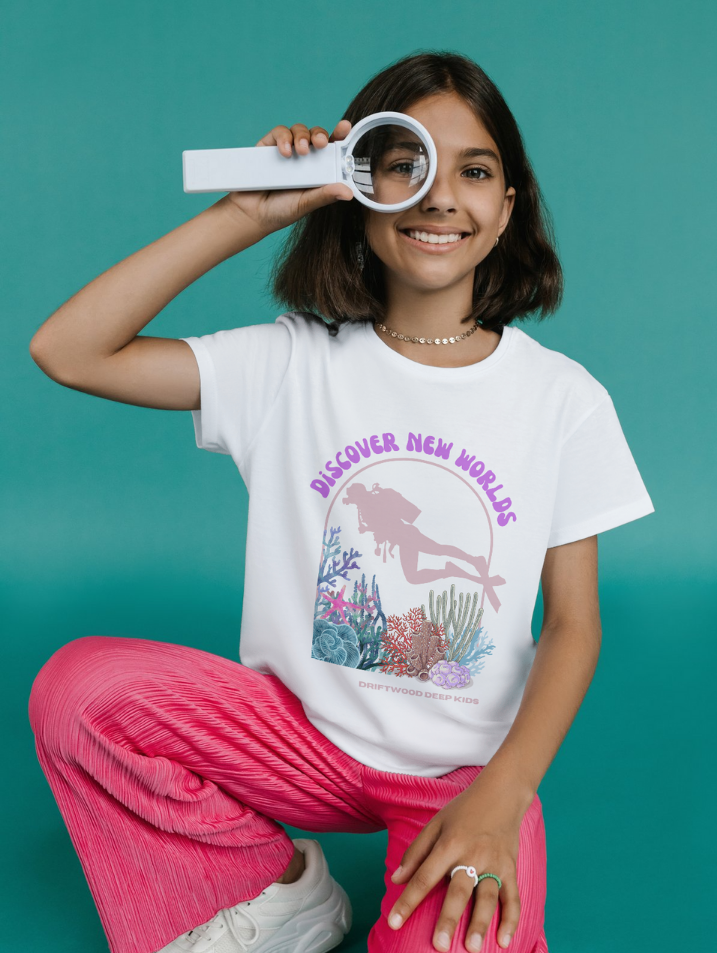 Girl wearing a white t-shirt with a mermaid graphic and text, sitting against a teal background.