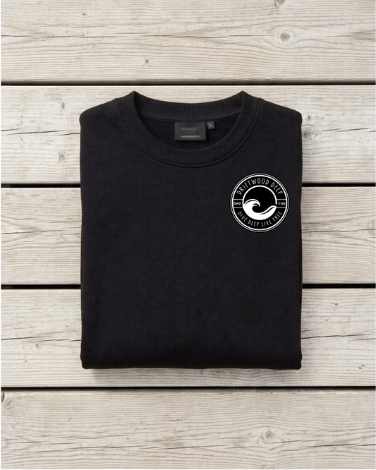 A folded black crewneck t-shirt with a white circular wave logo on the left chest, displayed flat on a light gray wooden plank background.