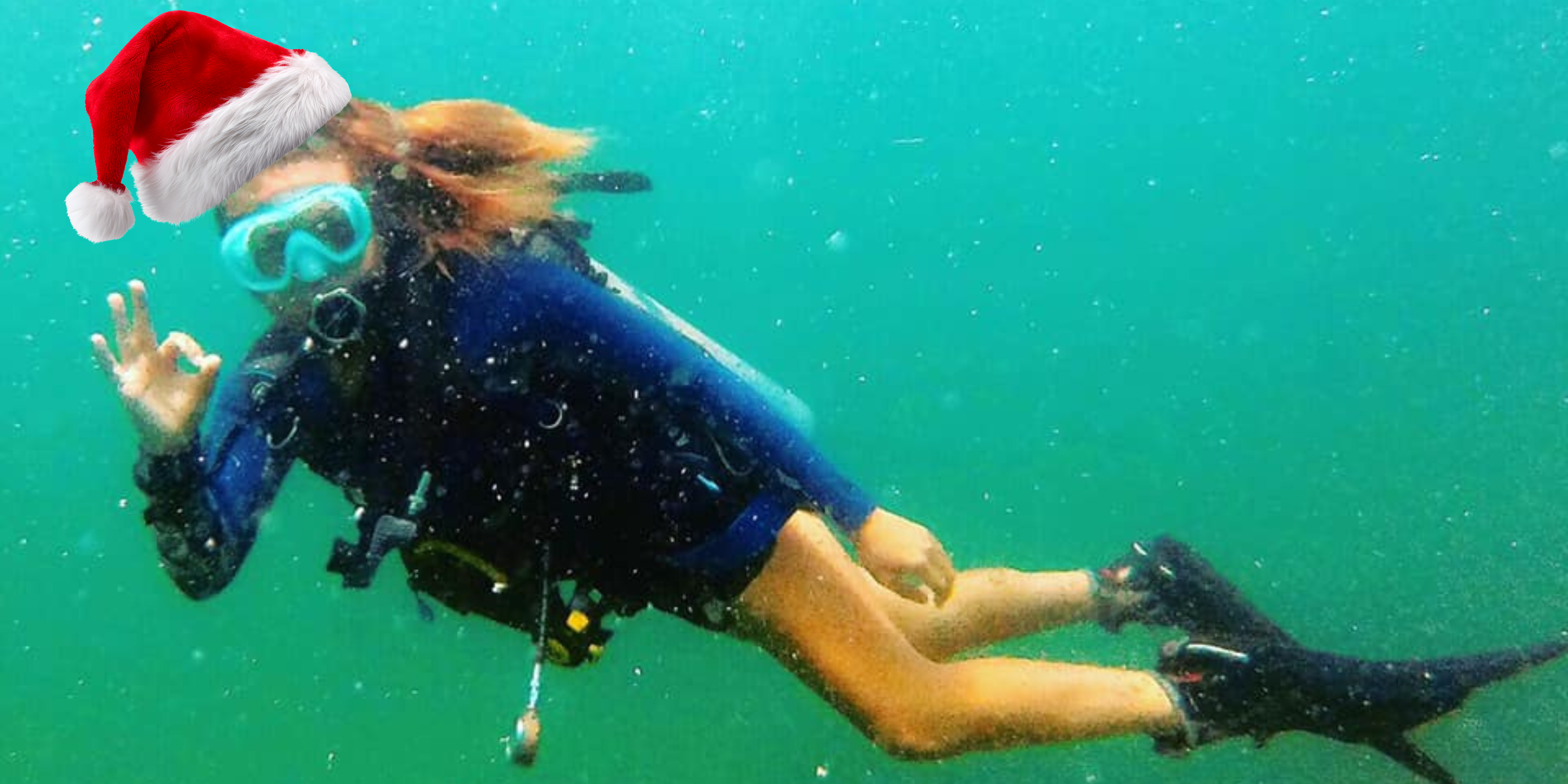 Person scuba diving underwater wearing a Santa hat