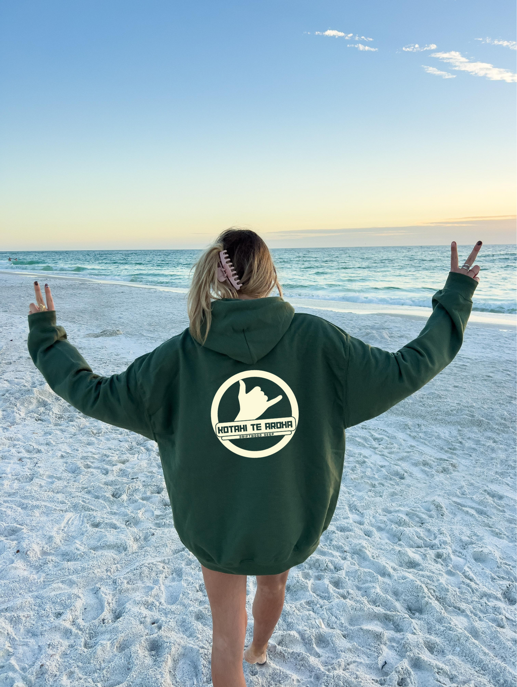 Person wearing a green hoodie with a logo on the beach
